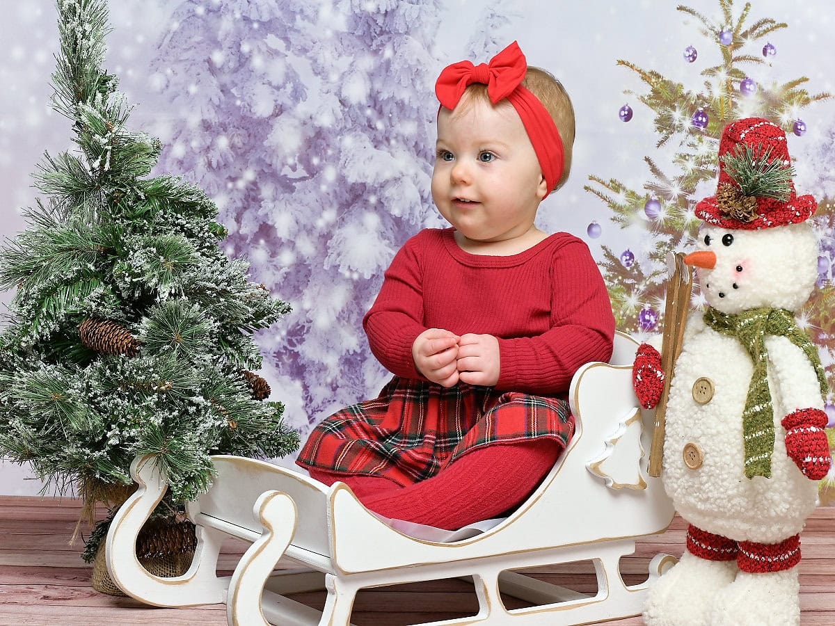 Photo of a baby sitting in a sleigh in a Christmas scene
