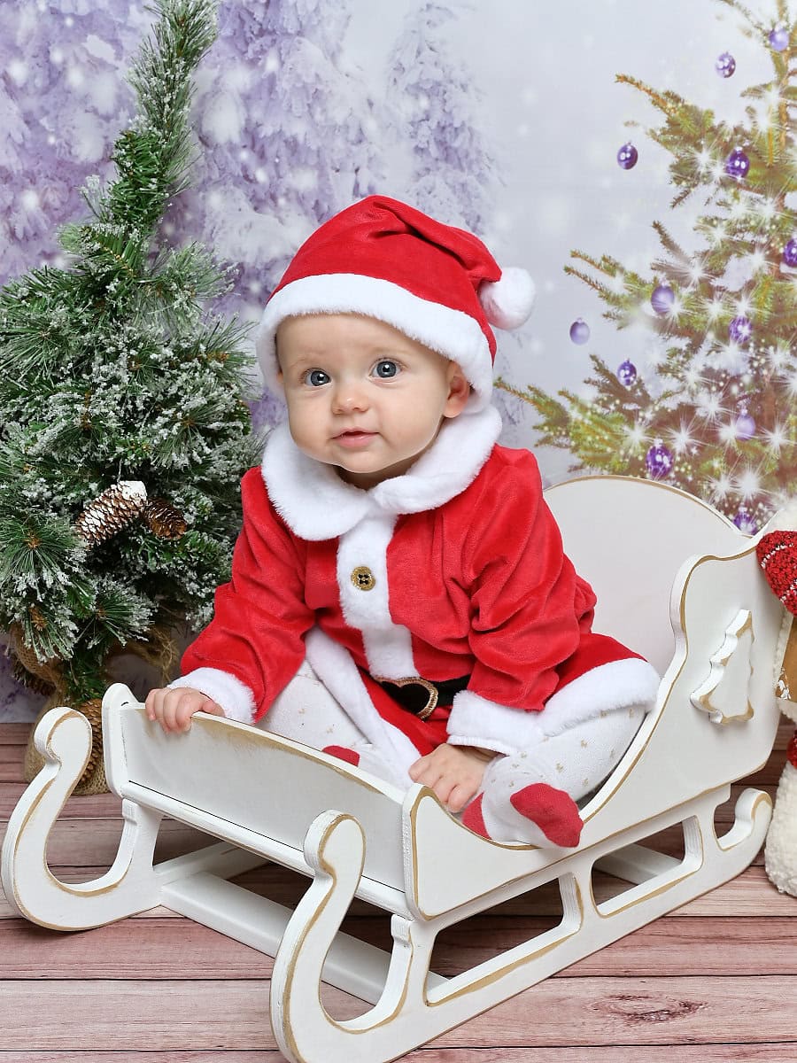 Photo of a baby dressed as Santa Claus sitting in a sleigh